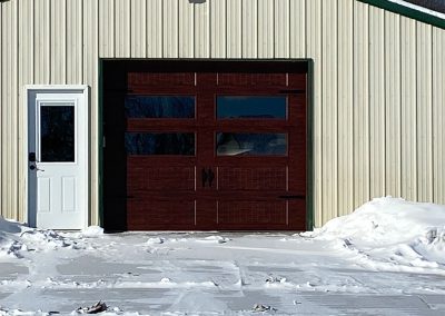 A commercial building with a brown garage door with a door on the right and snow on the ground.