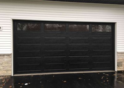 A home with white siding and a stone veneer with a black garage door and a wet driveway.