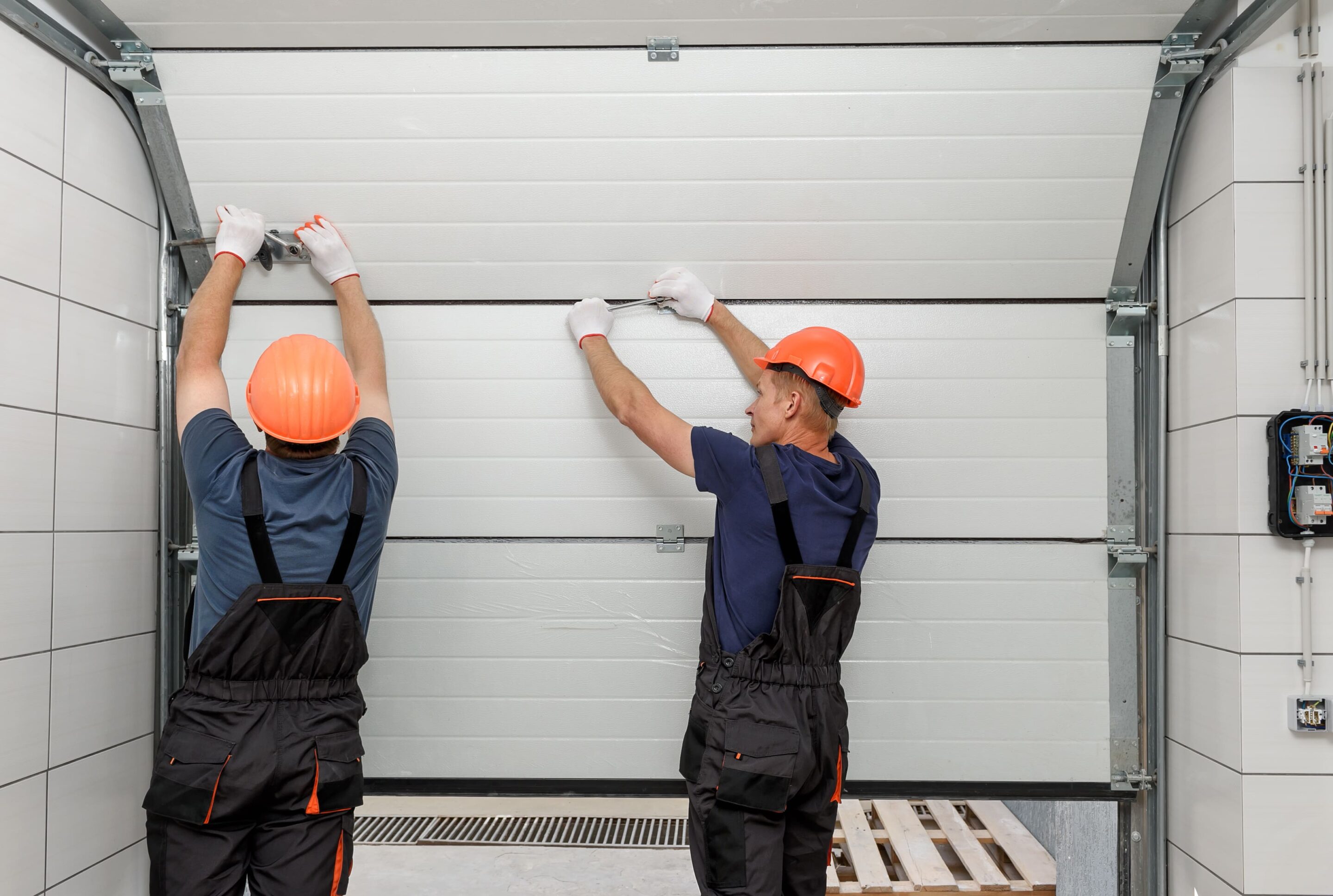 workers-are-installing-lifting-gates-garage (1) Technician installing garage door inside workshop.